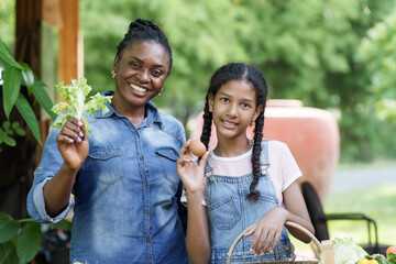 African teacher and asian student holding vegetables and egg while smiling in school gardening class with natural background, showing successful harvest of organic farming learning activity