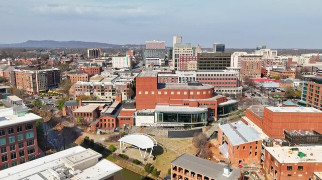 A view of downtown Greenville, South Carolina with the Reedy River and many brick buildings in the forefront and the Blue Ridge Mountains in the background.