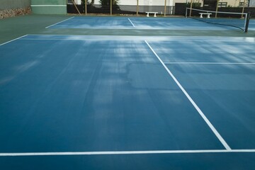 Flat design is showing empty blue hard tennis court with black net, chain-link fence, green wall