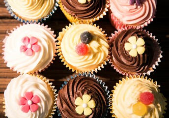 Nine cupcakes are sitting in flat design on wood tabletop with pastel liners and candy decorations