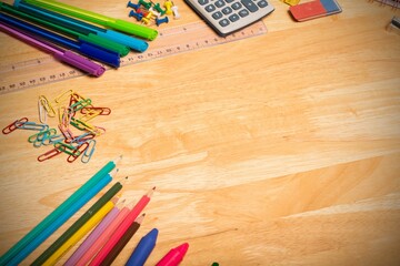Cluster of colored pencils, paperclips, pens and ruler is resting on left of light wooden desk