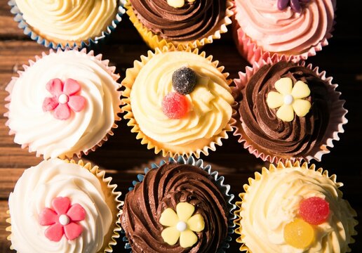 Naklejki Nine cupcakes are sitting in flat design on wood tabletop with pastel liners and candy decorations