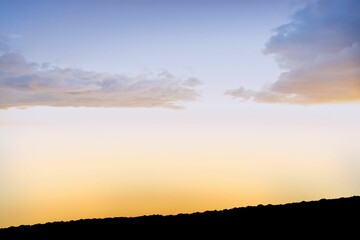 Gradient sky is shifting from warm golden yellow to pale blue in flat design, silhouetted ridge