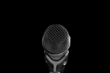Close-up black and white shot of a microphone in a studio or concert on stage, on a black background.