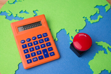 Red emergency push button and calculator on world map background. Global economy and financial...