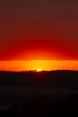 A stunning sunset displays a vibrant red sky along with a few silhouetted trees positioned in the foreground, creating a picturesque scene