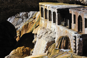 An exotic-looking stone building under a rock. An old castle covered in moss. Sewage flowing under an ancient stone building