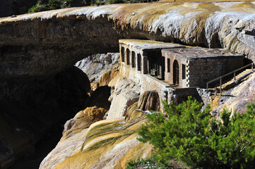 An exotic-looking stone building under a rock. An old castle covered in moss. Sewage flowing under an ancient stone building