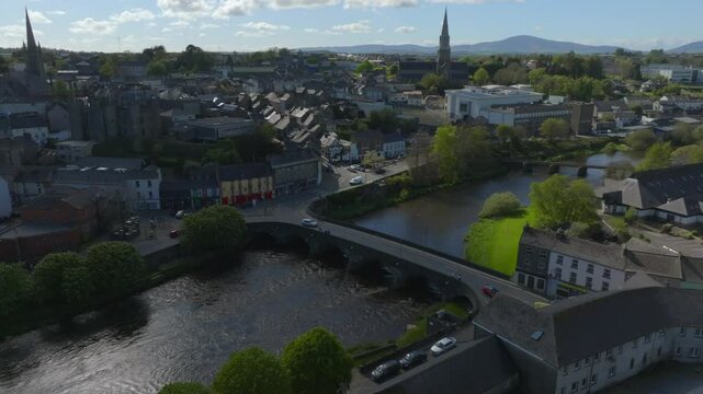 Enniscorthy, County Wexford, Ireland, April 2025. Drone establishing medium overview of bridge and castle connecting town across River Slaney as cloud shadow covers buildings.
