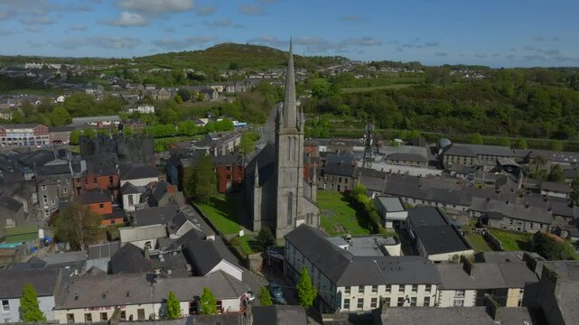 St. Mary's Church, Enniscorthy, County Wexford, Ireland, April 2025. Drone tracking right across front view of church with lush green hills and homes dotting the hillside.