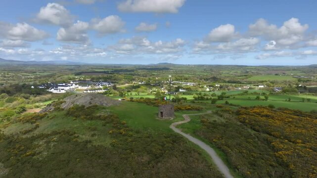 Vinegar Hill, Enniscorthy, County Wexford, Ireland, April 2025. Drone tilts up as cloud shadow covers stone tower monument and pulls back away revealing dirt path up to top of monument overlook point.