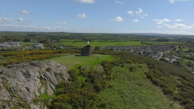 Vinegar Hill, Enniscorthy, County Wexford, Ireland, April 2025. Drone orbit and approach over rocky cliff face keeping tower monument centered underneath bright blue sunny sky.