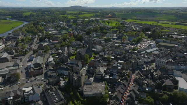 Enniscorthy, County Wexford, Ireland, April 2025. Drone panoramic aerial establishing overview of village roof tops ascending to show road network on sunny day.