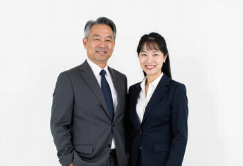 Experienced Asian male leader with young female professional, standing in suits against white background, symbolizing corporate collaboration and success.
