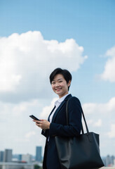 Dynamic Asian female executive smiles with smartphone in hand outdoors, reflecting urban business connectivity, professional confidence, and digital success.
