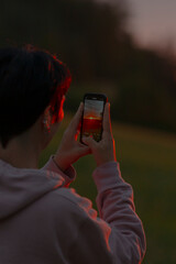 A person is capturing a beautiful image of a stunning sunset using their cell phone to preserve...