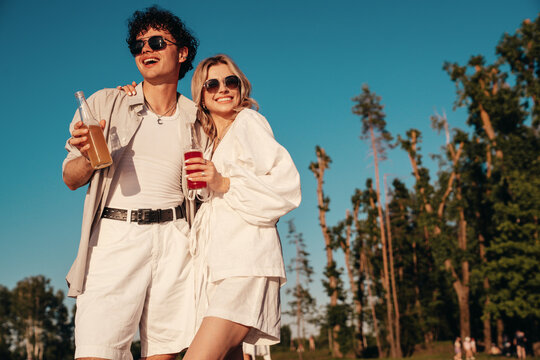 Young stylish friends posing at the seaside. Fashion man and two cute female dressed in casual summer clothes. Smiling models having fun. Cheerful women and guy outdoors, Hold and drink lemonade - Powered by Adobe