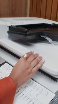 Vertical shot of young black female employee in elegant blouse making copies of documents while working in office