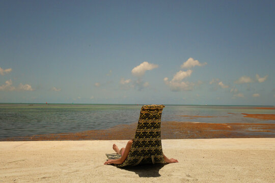 Behind young girl sitting in lounge chair on beach vibrant sky F