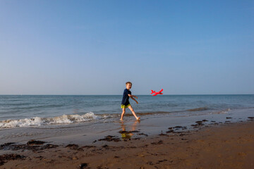 Little boy with sunhat playing with red airplane by the sea