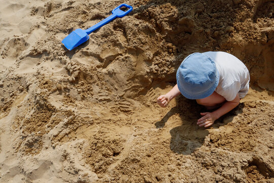 Small child digging in the sand on a warm beach day