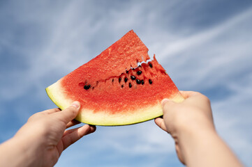 Holding a slice of watermelon with seeds against the sky.