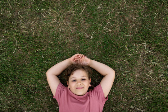 Girl resting on the grass with hands behind head.
