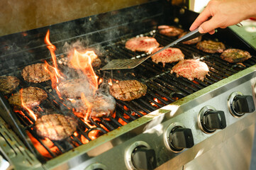 Person flipping burgers sizzling with flames on hot outdoor gas grill