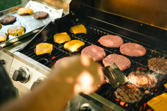 Father flipping cheeseburgers and patties grilling on outdoor barbecue