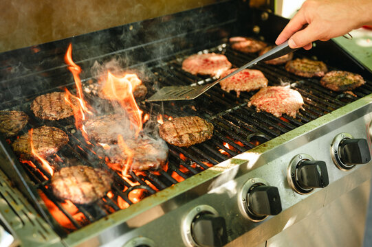 Person flipping burgers sizzling with flames on hot outdoor gas grill - Powered by Adobe