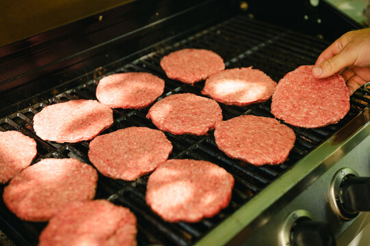 Person placing raw burger patties cooking on an outdoor gas grill - Powered by Adobe