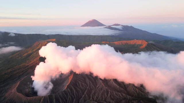 Aerial view of active Mount Bromo volcano emitting smoke with Mount Semeru in the distance at sunrise. Dramatic volcanic landscape in East Java, Indonesia.