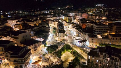 Drone shot of Tropea at night with glowing buildings and dark sea in summer season