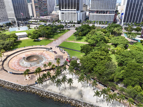 Aerial View of a vibrant urban park where lush green trees meet the stark architectural lines of skyscrapers, all set against a serene waterfront, Miami, Florida, United States
