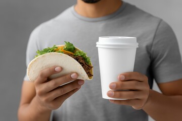 Man holding a delicious taco filled with fresh ingredients in one hand and a disposable coffee cup in the other, showcasing a casual dining experience with food and drink