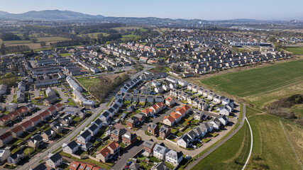 Aerial view of neat rows of houses with colorful rooftops nestled amidst green fields under a clear sky in Newton Village, Dalkeith, Scotland, United Kingdom.