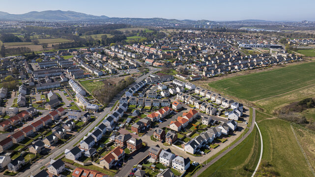 Aerial view of neat rows of houses with colorful rooftops nestled amidst green fields under a clear sky in Newton Village, Dalkeith, Scotland, United Kingdom.