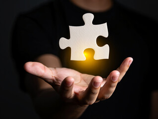 Holding a glowing puzzle piece in hand shows a solution or connection concept with dark background for creativity