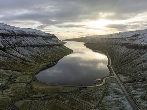 Aerial view of a serene lake nestled between snow-dusted mountains under a luminous sky, capturing the stark beauty of the landscape, Tj&Atilde;&cedil;rnuv&Atilde;&shy;k, Streymoy, Faroe Islands.
