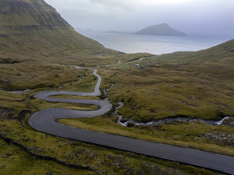 Aerial view of a winding road snaking through the rugged, grassy Faroese landscape towards the sea, Tj&Atilde;&cedil;rnuv&Atilde;&shy;k, Streymoy, Faroe Islands.
