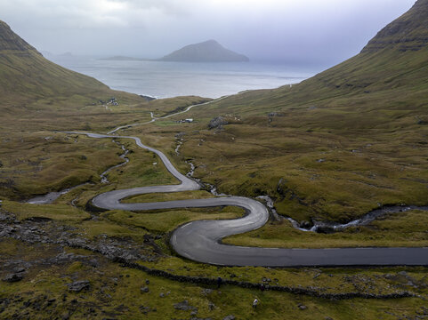 Aerial view of a winding road snaking through a valley, connecting to the sea under a misty sky, Tj&Atilde;&cedil;rnuv&Atilde;&shy;k, Streymoy, Faroe Islands.