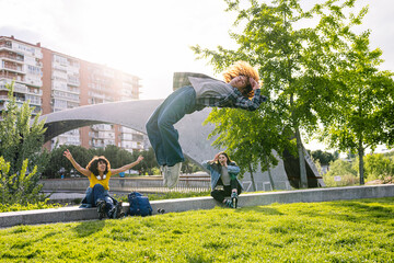 Friends enjoying a sunny day in the park, one performing a backflip while wearing casual clothes,...