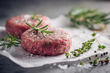 Two raw burger patties with thyme and reosemary on white