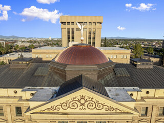 Aerial view of the copper dome of the Arizona State Capitol building gleams beneath a bright sky, flanked by modern architecture, Phoenix, Arizona, United States.