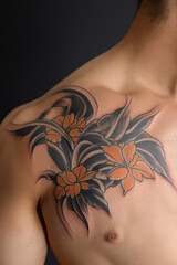 Large floral tattoo black and orange flower design covers male shoulder and chest intricate leaf pattern bold lines modern body art confident expression smooth skin