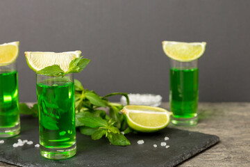 Sweet refreshing mint liqueur, with ice and mint leaves on table background, Shots with lime slice...