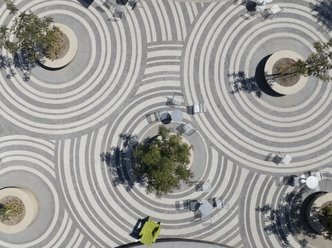 Aerial view of concentric circles of light and dark stone converge around trees and seating in a modern urban plaza, Scottsdale, Arizona, United States.