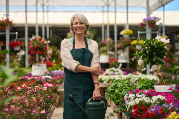 Senior woman gardener working in greenhouse, holding watering can