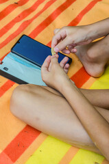 Child sits on striped blanket holding snack chip and smartphone during summer leisure. High quality...