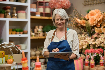 Smiling senior saleswoman using digital tablet in flower shop